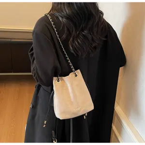 Beige suede bucket bag with metal chain strap and drawstring closure for stylish commute.