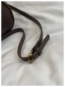 Detalle de correa de bolso de hombro de ante marrón, hebilla de metal, accesorio elegante diario.