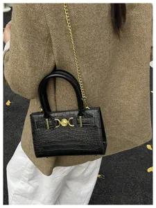 Detailopname van een zwarte schoudertas met krokodillenprint en luxe gouden ketting.