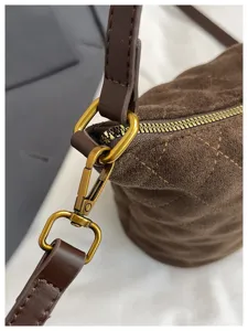 Primer plano de bolso saco de ante marrón con herrajes de bronce vintage y textura acolchada.
