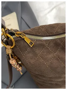 Detalle de bolso saco de ante marrón, con patrón acolchado, cremallera dorada y abalorio de cuentas.