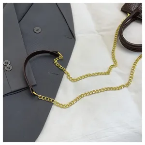 Gedetailleerd overzicht van bruine krokodillenpatroon handtas met gouden ketting en blazer.