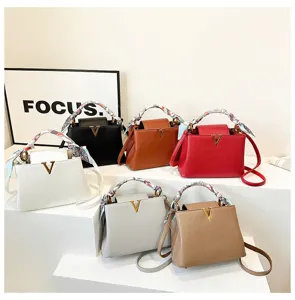 Versatile litchi grain handbag with metal V clasp and stylish scarf handle detail.