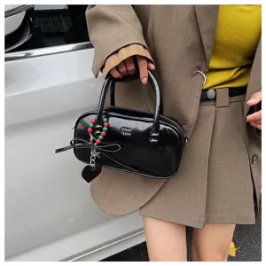 Detailaufnahme einer schwarzen Lackleder Bowlingtasche mit Perlenanhänger und Griffen.