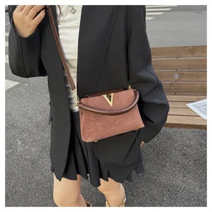 Detail shot of retro brown suede shoulder bag with metal V logo, stylish casual street look.