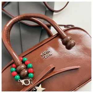Nahaufnahme der braunen Lackleder-Bowlinghandtasche mit Perlenanhänger und Metallstern.