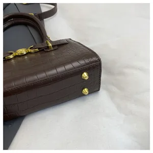 Detailopname van donkerbruine kroko lederen handtas met gouden metalen beslag en beschermvoetjes.