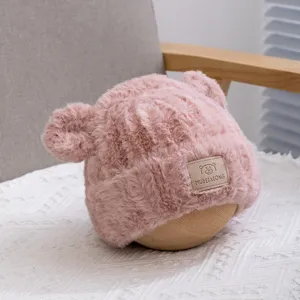Close-up detail of fluffy pink children's winter plush hat with cute bear ears and small logo.