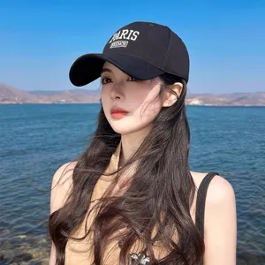 Detail shot of a black cotton baseball cap with stylish white embroidery outdoors by the water.
