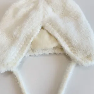 Close-up detail of fluffy white baby earflap hat showing soft plush texture and cozy lining.