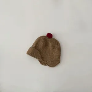 Close-up detail view of cute toddler brown knit hat featuring red pom-pom and ear flaps.