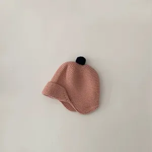 Close-up detail of cute pink knit baby toddler beanie hat with earflaps and pom-pom.