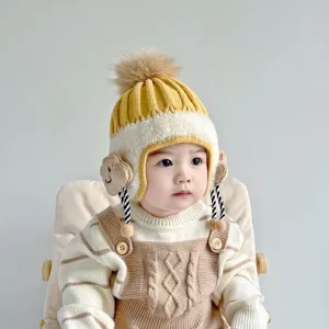 Detailed view of cute baby winter knit hat with pom-pom, yellow white earflap and braids.
