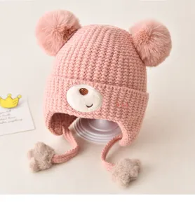 Cute pink baby knit hat with double pom-poms and bear face design for winter warmth.