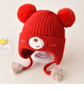 Detailed close-up of adorable red knit baby winter hat with cute bear face and dual pom poms.