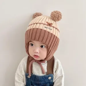Cute baby winter knitted ear-flap hat with double pom-poms and bear embroidery detail view.