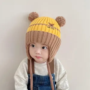 Cute baby winter knit earflap hat detail showing fluffy pom-poms and lovely bear embroidery.
