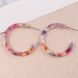 Gros plan détaillé de boucles d'oreilles créoles en acrylique coloré avec belle texture.