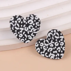 Primer plano detallado de pendientes de acrílico con diseño de corazón de leopardo blanco y negro.