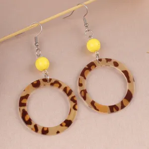 Close-up detail of vintage leopard print acrylic hoop earrings with bright yellow bead accent.