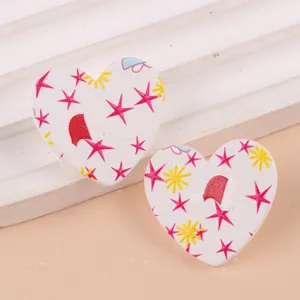 Primer plano de pendientes de tuerca acrílicos con corazón navideño y detalles.