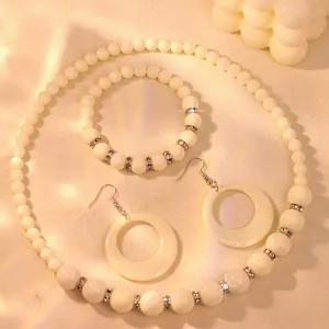 Close up detail of cream bead necklace bracelet and hollow round pendant earrings jewelry set.