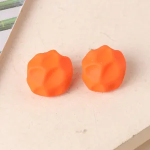 Primer plano pendientes de botón geométricos irregulares naranja, diseño mate.