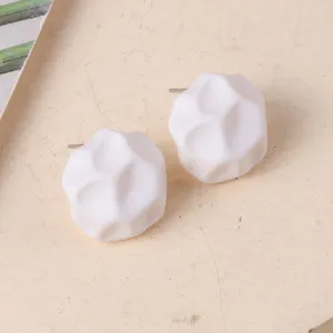 Primer plano de pendientes de botón geométricos blancos con textura de roca facetada.