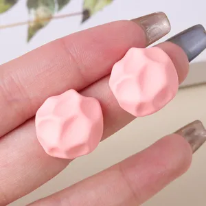 Primer plano de pendientes de tuerca de acrílico geométrico irregular rosa con acabado mate.