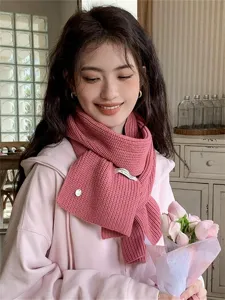 Close-up detail of cozy pink knitted scarf worn by model in warm indoor lifestyle scene.