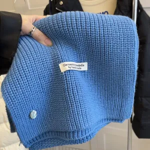 Knit scarf detail shot showing soft blue wool texture and handmade label decoration.