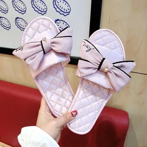 Gros plan de pantoufles plates en satin rose avec nœud, broderie et pendentif brillant.