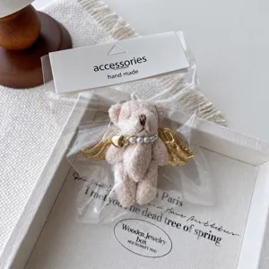 Adorable plush angel bear keychain featuring pearl necklace and gold wings for bag decor.