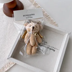 Cute plush bear keychain with pearl necklace and wings, detailed close-up shot for bag decor.