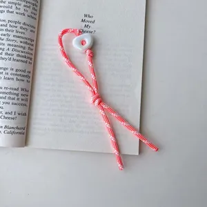 Close-up detail view of pink woven phone lanyard charm with white bead on book page.