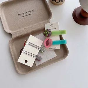 Detail shot of sweet resin fruit side hair clips with metal pins arranged in a paper box tray.