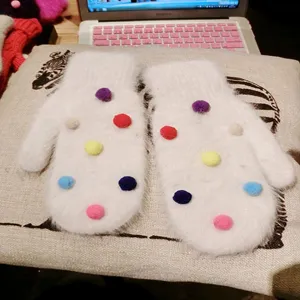 White fluffy rabbit fur mittens with colorful pom poms, cute winter warm gloves detail.