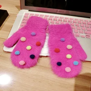Close-up detail view of cute fuzzy pink mittens featuring colorful pom-poms on cozy desk.