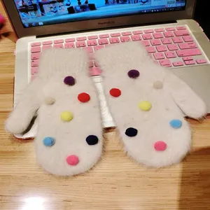 Fluffy white rabbit hair mittens detail featuring cute colorful pom-poms and warm winter design.