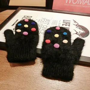 Close-up view of black fuzzy knit mittens featuring colorful plush pom-pom decorations.