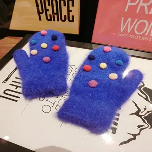Close-up of cozy blue fuzzy mittens decorated with colorful pom poms on styled background.