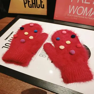 Detail shot of red fluffy winter mittens featuring cute colorful pom-pom decorations.
