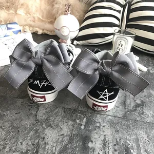Black canvas sneakers featuring oversized grey bow detail, trendy low-top casual shoes.