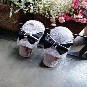 Close-up of grey fluffy women slippers featuring an elegant black bow and pearl pendant detail.
