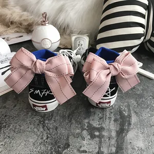 Detail shot of black high-top sneakers featuring a large pink bow on the heel, stylish design.