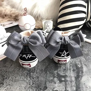 Detailed shot of trendy black canvas sneakers featuring oversized gray bows on the back.