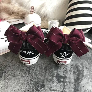 Black canvas skate sneakers featuring oversized wine red bow ribbons and heel graffiti.