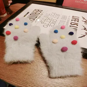 Detail view of fuzzy winter mittens featuring colorful fluffy pom-poms on grey soft fabric.
