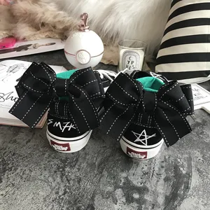 Black canvas sneakers detail showing large heel bow, embroidered star and brand text on back.