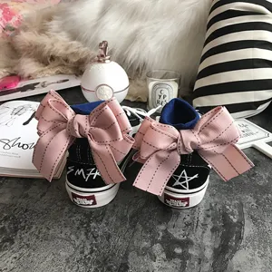 Close-up detail of black canvas skate shoes featuring a large pink bow on the back heel.